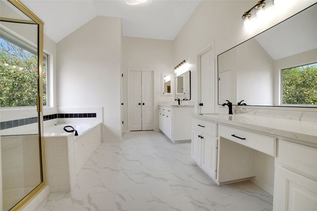 Full bath featuring lofted ceiling, marble look tiles, two vanities, a garden tub, and a stall shower | Image 23
