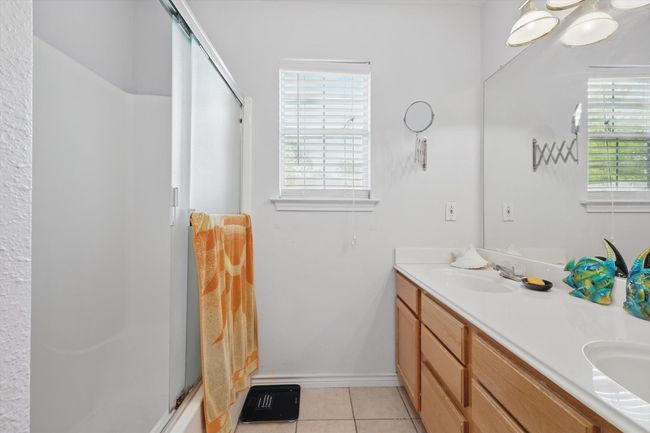 Full bathroom featuring baseboards, a sink, double vanity, tile patterned floors, and a shower with shower door | Image 25