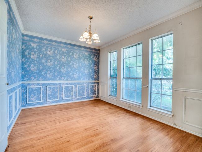 Empty room with a chandelier, wood finished floors, a textured ceiling, wallpapered walls, and crown molding | Image 8