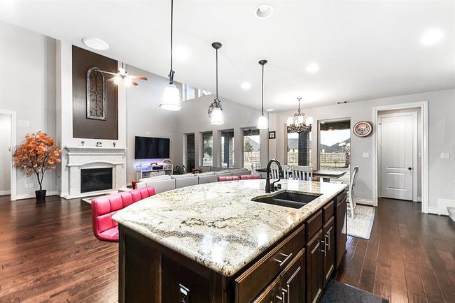 This spacious open-concept home features a modern kitchen with beautiful granite countertops and a stunning island as the focal point. The sink is conveniently positioned to face the living room, breakfast room, and backyard, offering a seamless connection between the spaces. The kitchen is beautifully illuminated with pendant lighting and recessed lighting, creating a bright, welcoming atmosphere perfect for both cooking and entertaining. | Image 16