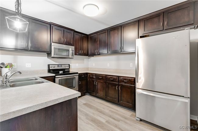 Kitchen with appliances with stainless steel finishes, a sink, light wood-type flooring, and dark brown cabinets | Image 7