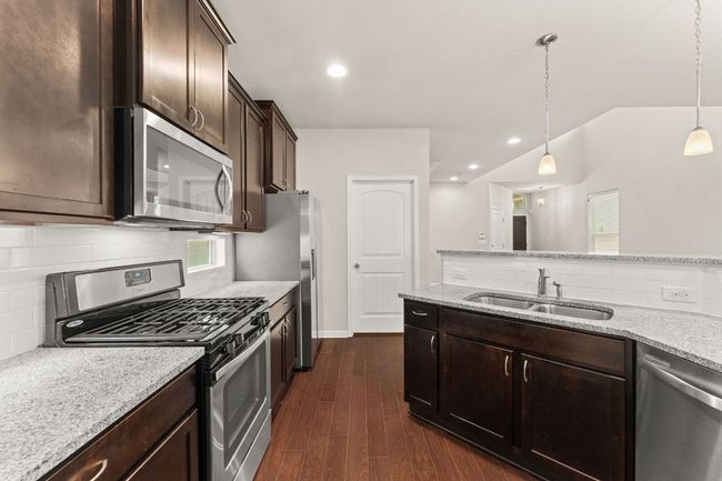 Kitchen featuring appliances with stainless steel finishes, a sink, dark brown cabinets, decorative backsplash, and dark wood-style flooring | Image 7