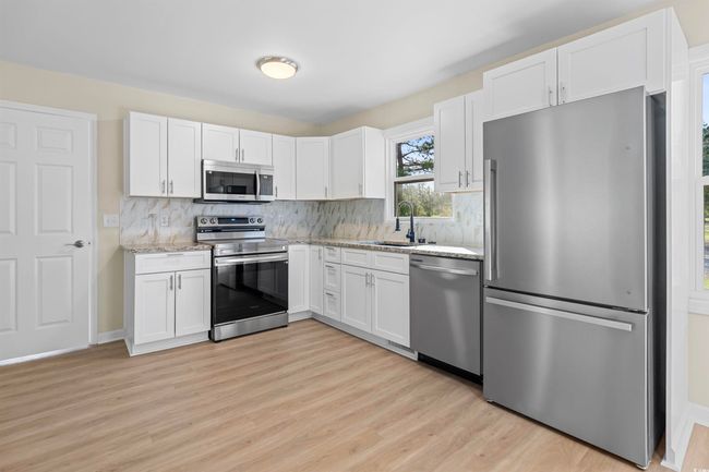 Kitchen with appliances with stainless steel finishes, light wood-type flooring, light stone counters, decorative backsplash, and white cabinetry | Image 21