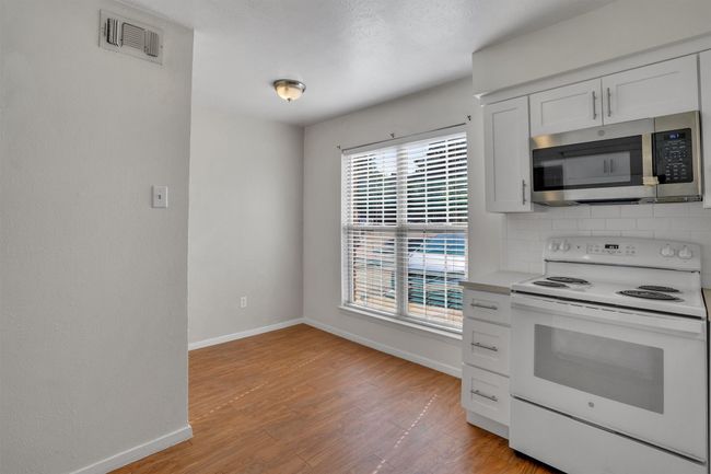 Kitchen with white electric range oven, stainless steel microwave, light wood-type flooring, decorative backsplash, and light countertops | Image 13
