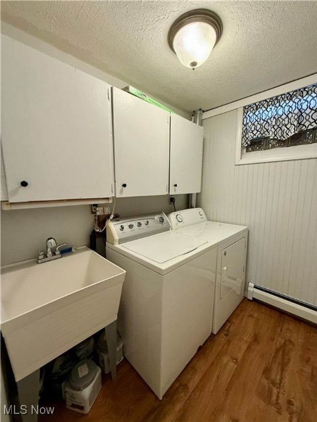 Laundry room with a textured ceiling, a baseboard heating unit, separate washer and dryer, cabinet space, and wood finished floors | Image 38
