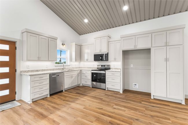 Kitchen with appliances with stainless steel finishes, a sink, high vaulted ceiling, light wood-type flooring, and light stone counters | Image 14