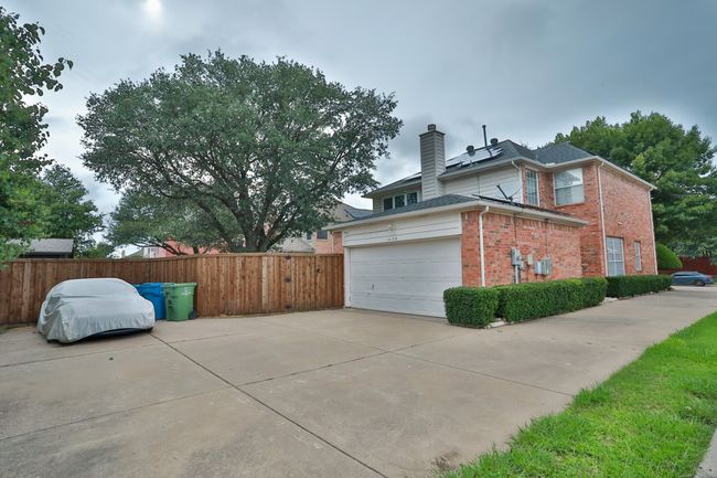 View of side of home featuring brick siding, a chimney, an attached garage, concrete driveway, and solar panels | Image 23