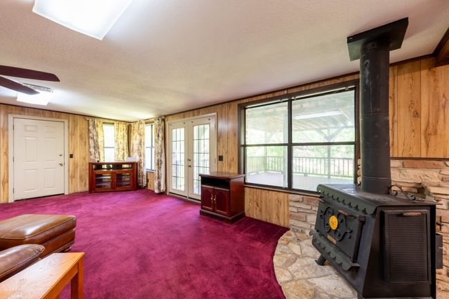 Carpeted living room featuring wooden walls, a wood stove, a textured ceiling, ceiling fan, and french doors | Image 20