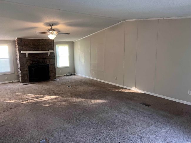 Unfurnished living room with crown molding, ceiling fan, carpet flooring, a stone fireplace, and a textured ceiling | Image 5