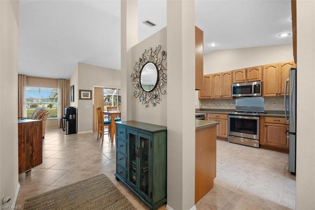 Kitchen featuring light tile patterned flooring, tasteful backsplash, visible vents, appliances with stainless steel finishes, and lofted ceiling | Image 14