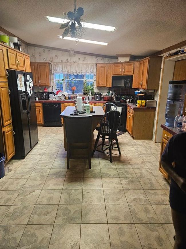 Kitchen with black appliances, light tile patterned floors, lofted ceiling, a center island, and ceiling fan | Image 25