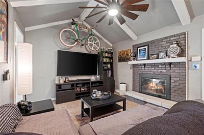 Living room featuring ceiling fan, a fireplace, vaulted ceiling with beams, and carpet | Image 2