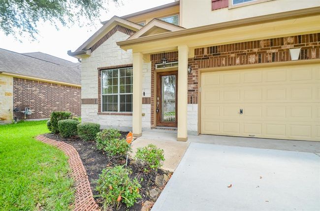 This home features a welcoming entrance with a covered porch, decorative brickwork, and a spacious attached garage. The well-maintained front yard includes neatly trimmed shrubs and a lush lawn, creating a charming curb appeal. | Image 4