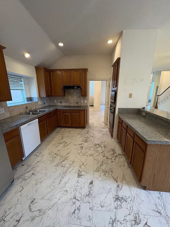 Kitchen featuring white dishwasher, dark countertops, tasteful backsplash, brown cabinets, and lofted ceiling | Image 13