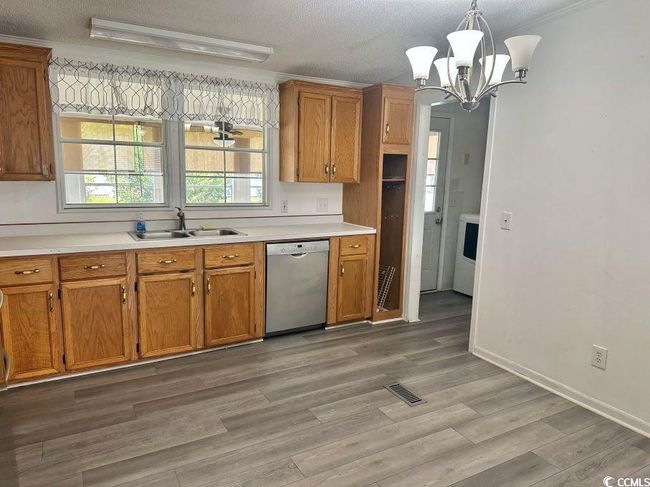 Kitchen featuring stainless steel appliances, dishwasher, a sink, a chandelier, brown cabinetry, and light countertops | Image 6