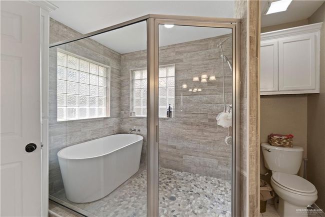 Bathroom with a freestanding bath, a shower stall, toilet, and tile walls | Image 4