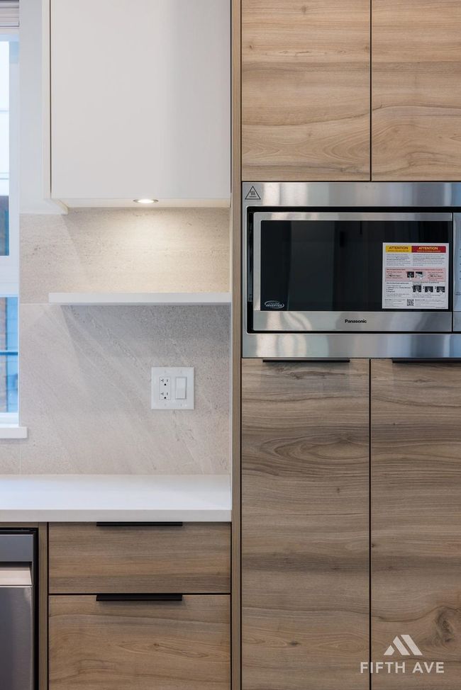 Kitchen view of modern cabinets, stainless steel microwave, white cabinets, and light countertops | Image 9