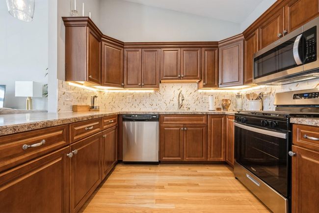 Kitchen with light stone counters, stainless steel appliances, backsplash, vaulted ceiling, and light wood-style floors | Image 7