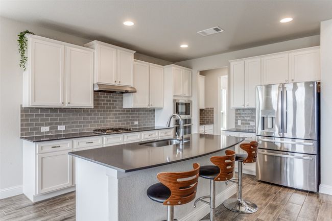 Kitchen featuring stainless steel appliances, dark countertops, wood finished floors, under cabinet range hood, and white cabinetry | Image 5