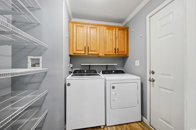 Laundry area featuring cabinet space, crown molding, washing machine and clothes dryer, a textured ceiling, and wood finished floors | Image 11