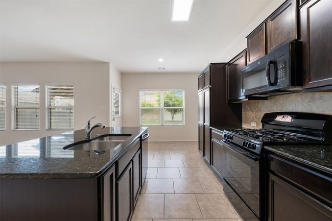 Kitchen featuring black appliances, a sink, dark stone counters, decorative backsplash, and dark brown cabinetry | Image 10