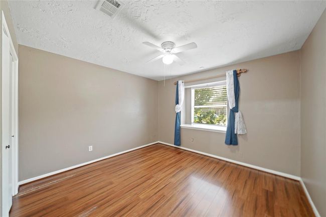 A third bedroom features a ceiling fan, wood like flooring, and a window. | Image 23