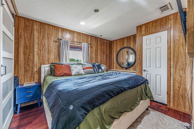 Bedroom featuring wood walls, wood finished floors, visible vents, and a textured ceiling | Image 22