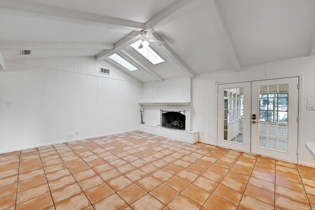 Unfurnished living room with french doors, a brick fireplace, visible vents, lofted ceiling with skylight, and ceiling fan | Image 6