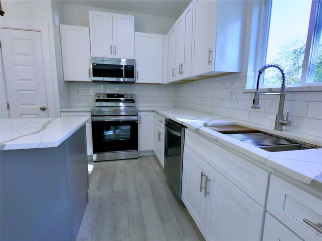 Kitchen featuring white cabinets, a sink, light wood-style floors, decorative backsplash, and appliances with stainless steel finishes | Image 6