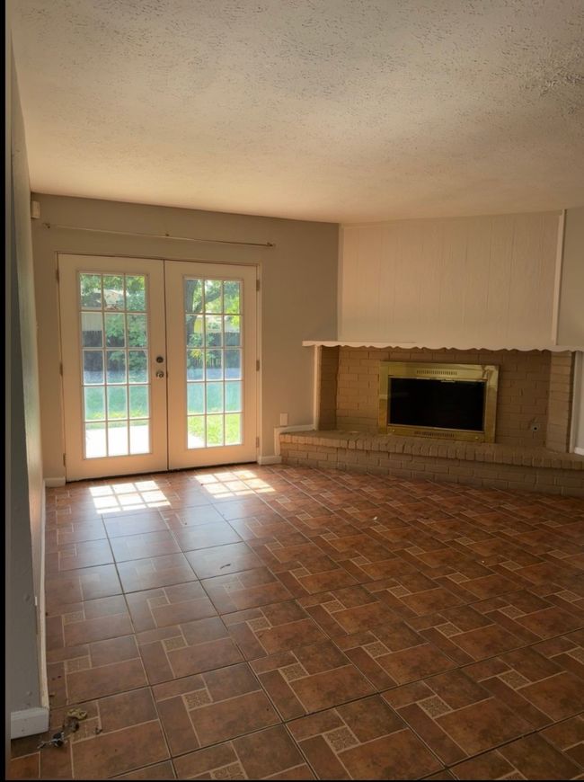 Unfurnished living room featuring a textured ceiling, a brick fireplace, and french doors | Image 5