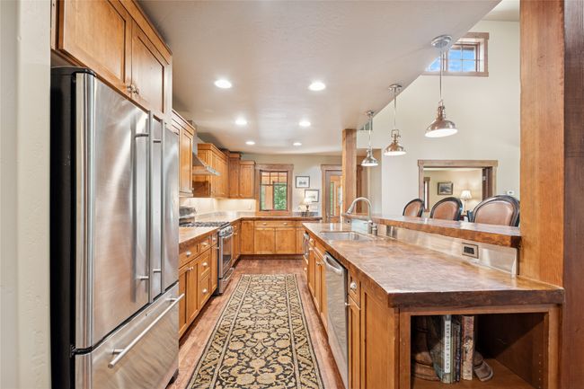Kitchen featuring stainless steel appliances, light wood-style flooring, recessed lighting, brown cabinetry, and decorative light fixtures | Image 23