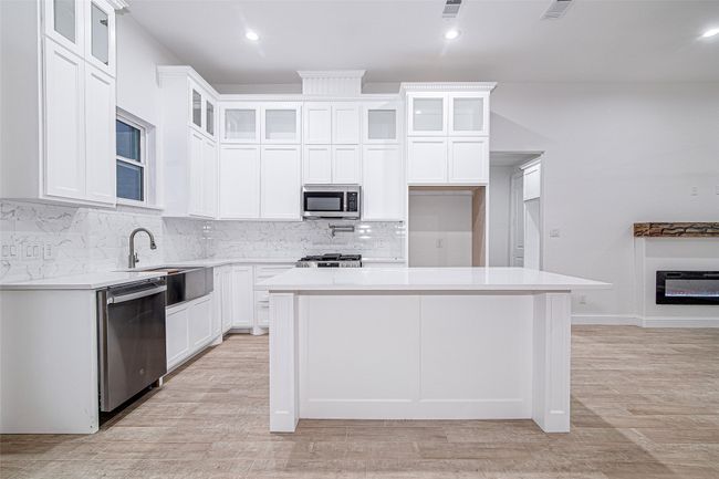 Kitchen featuring stainless steel appliances, a sink, a center island, backsplash, and light countertops | Image 7