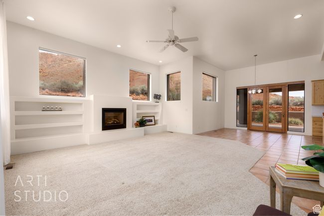 Living room featuring carpet floors, a glass covered fireplace, built in shelves, ceiling fan with notable chandelier, and recessed lighting | Image 14