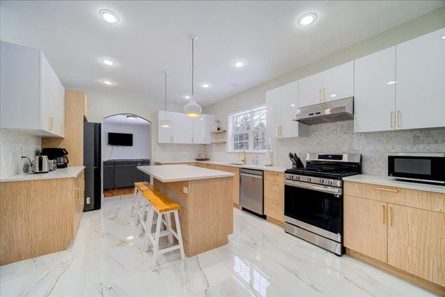 Kitchen with stainless steel appliances, under cabinet range hood, a kitchen bar, a kitchen island, and open shelves | Image 10