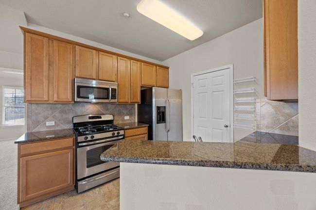 Kitchen with dark stone countertops, stainless steel appliances, tasteful backsplash, and a peninsula | Image 12