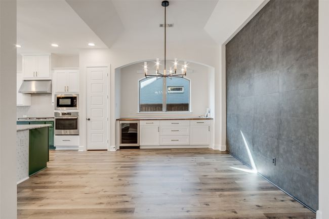 Kitchen featuring appliances with stainless steel finishes, wine cooler, white cabinetry, a chandelier, and light wood-style flooring | Image 9