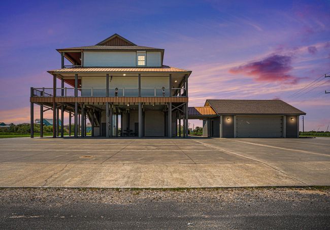 Stunning twilight view of elevated beach home with wraparound deck, spacious parking, and detached garage. Perfect for sunset relaxation. | Image 50