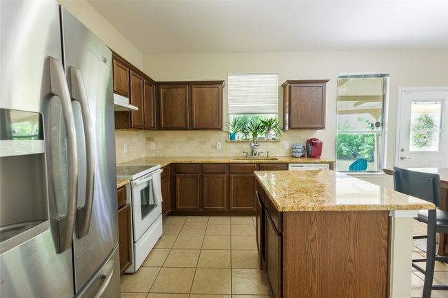 Kitchen featuring white appliances, a center island, under cabinet range hood, a sink, and backsplash | Image 7