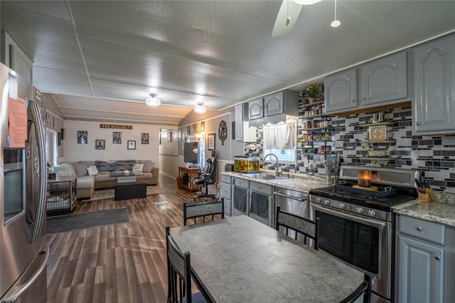 Kitchen with appliances with stainless steel finishes, a sink, gray cabinetry, tasteful backsplash, and lofted ceiling | Image 4
