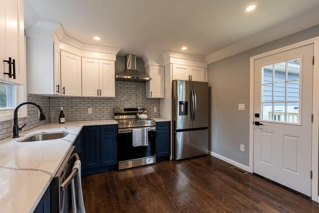Kitchen with light stone counters, visible vents, wall chimney exhaust hood, stainless steel appliances, and a sink | Image 10