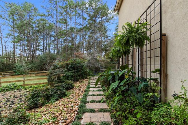 Lined with lush greenery, climbing vines and decorative trellises, this inviting pathway leads to a private, fenced section of the property and creates a peaceful transition between the home and the expansive outdoor areas. The owners hand-placed cobblestones on the pathways throughout the property enhancing its distinctive, old-world charm. | Image 38