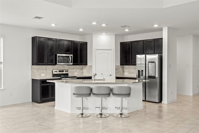 Kitchen featuring stainless steel appliances, dark cabinets, backsplash, an island with sink, and recessed lighting | Image 12
