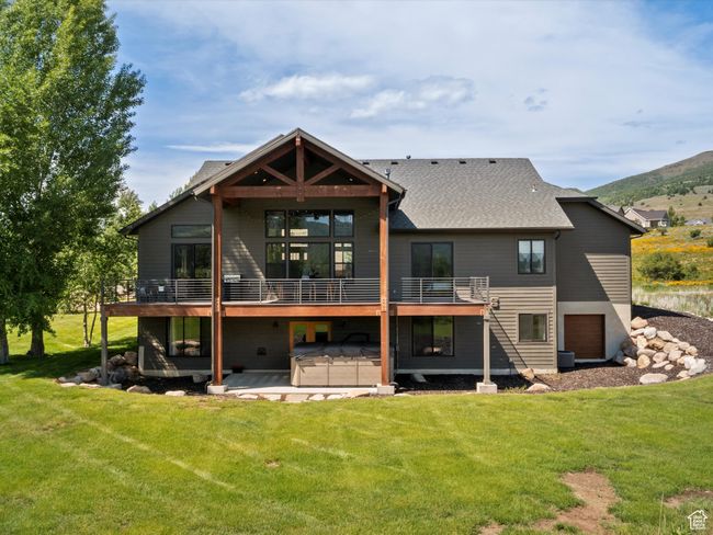 Rear view of property featuring a hot tub, a lawn, a patio area, and an attached garage | Image 6