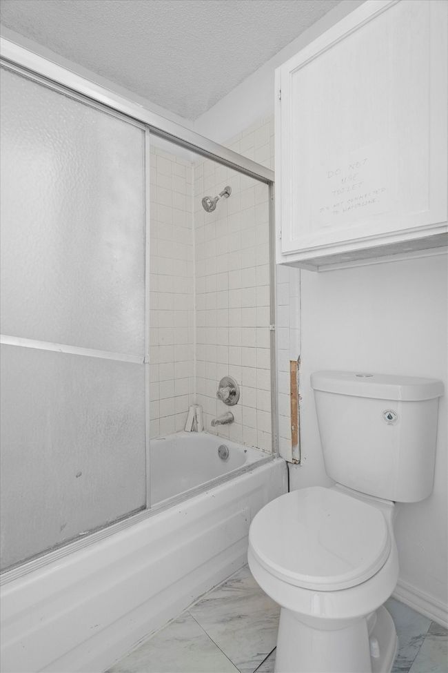 Full bath featuring marble look tiles, combined bath / shower with glass door, and a textured ceiling | Image 15