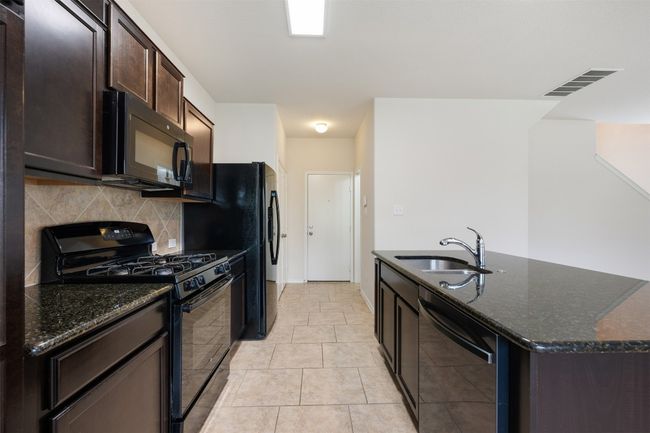 Kitchen with black appliances, decorative backsplash, a center island with sink, and dark stone countertops | Image 17