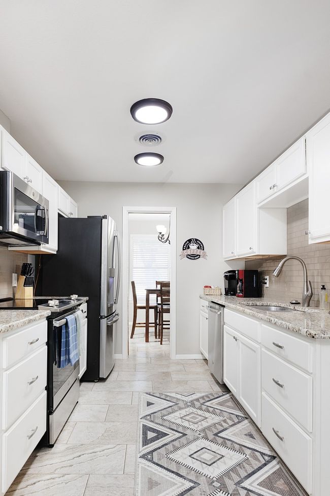 Kitchen with backsplash, visible vents, white cabinets, and stainless steel appliances | Image 12