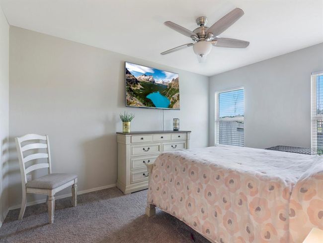 Step into the primary bedroom with soft gray walls and carpet, featuring a ceiling fan. Natural light filters through two windows, creating a bright and inviting atmosphere. | Image 13