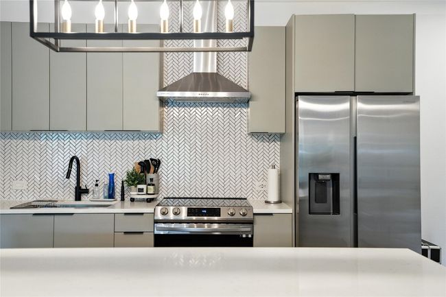 Kitchen with stainless steel appliances, gray cabinetry, backsplash, wall chimney range hood, and light countertops | Image 12