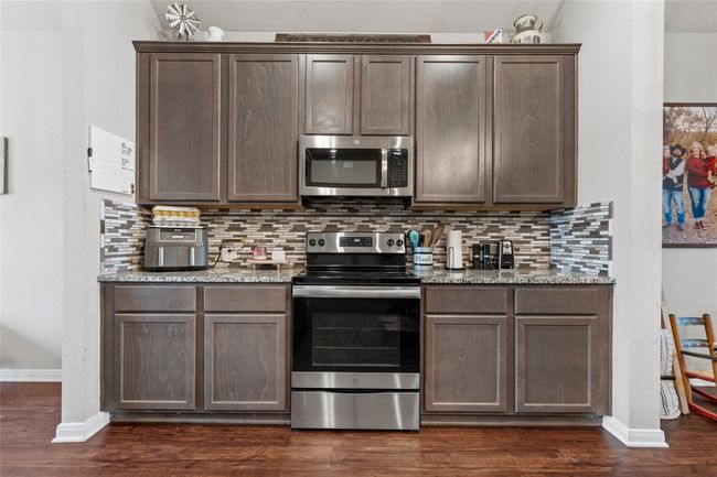 Kitchen featuring stainless steel appliances, dark brown cabinets, baseboards, backsplash, and dark wood-style floors | Image 13