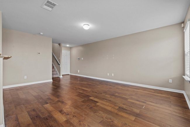 Unfurnished room featuring baseboards, wood finished floors, visible vents, and stairway | Image 5